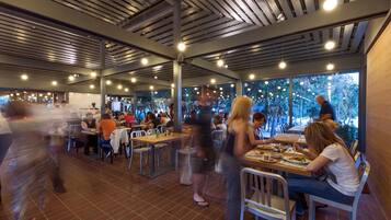 Un restaurant au décor moderne, avec des plafonds apparents et de grandes fenêtres offrant une vue sur l’extérieur.