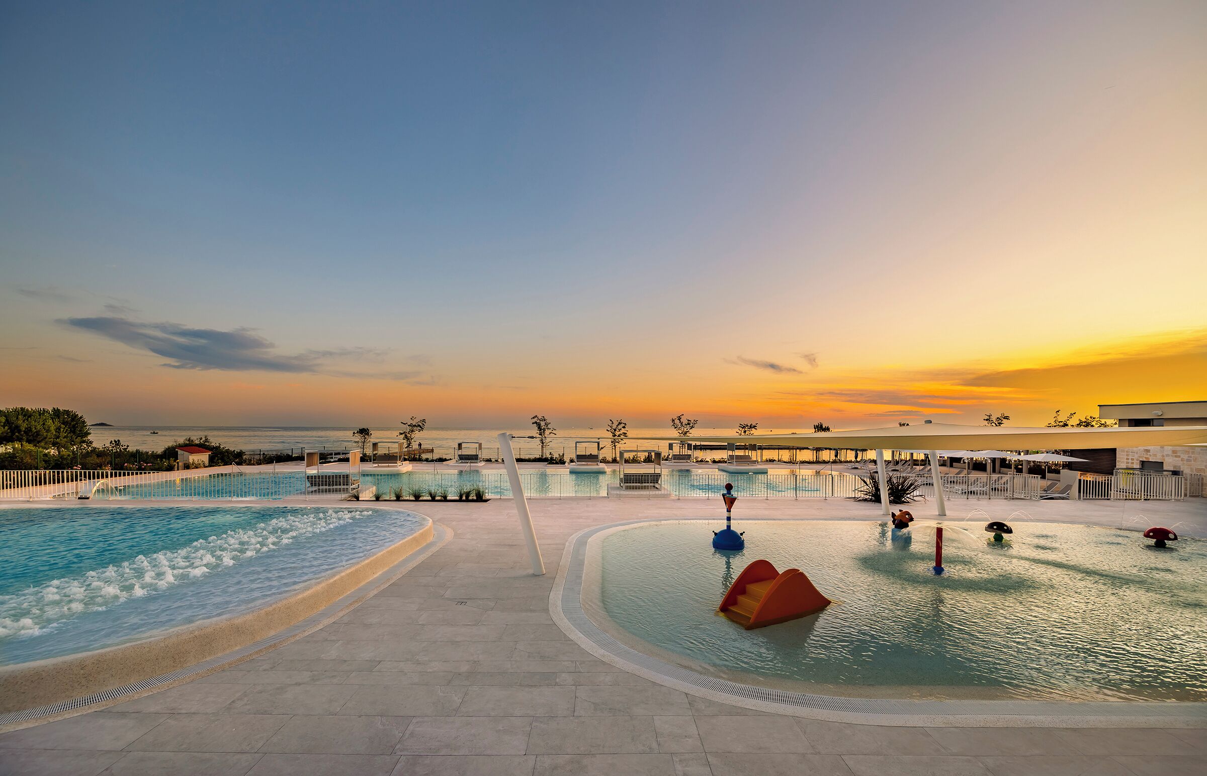 A pool area with a sunset view, multiple water features, and a clear sky.