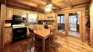A wooden cabin interior with a kitchen, dining table, and chairs. - Leave the stress behind!- private hot tub, pet and motorcycle friendly, let peace and nature surround you! 2 Bedroom Home by RedAwning (Tellico Plains)
