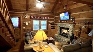 A cozy cabin interior with a fireplace, wooden walls, a ceiling fan, and a television. - Leave the stress behind!- private hot tub, pet and motorcycle friendly, let peace and nature surround you! 2 Bedroom Home by RedAwning (Tellico Plains)