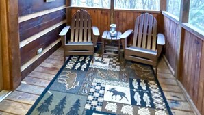 A cabin interior with wooden walls, two Adirondack chairs, a small table, and a patterned rug. - Leave the stress behind!- private hot tub, pet and motorcycle friendly, let peace and nature surround you! 2 Bedroom Home by RedAwning (Tellico Plains)