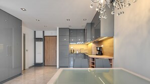 A modern kitchen with a glass dining table, grey cabinets, and a wooden cabinet.
