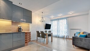 A modern kitchen with grey cabinets, a dining table with chairs, a coffee machine, and a chandelier.