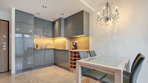 A modern kitchen with grey cabinets, a glass dining table, and a chandelier.