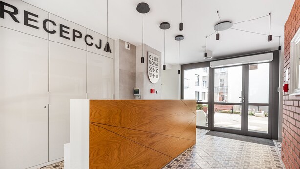 A reception area with a wooden reception desk, a white wall with a sign reading "RECEPCJJA", and a patterned floor.
