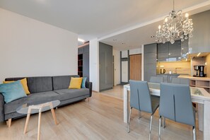 A modern living room with a grey sofa, a glass coffee table, and a dining area with grey chairs. - Happy Stay OldNova Deluxe Apartment 366 (Gdansk)