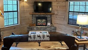 A cozy cabin interior with a stone fireplace, wooden walls, a flat-screen TV, a sofa, and a table. - Private and Perfect! - hot tub, king bed, fireplace - dog and motorcycle friendly Studio Cabin by RedAwning (Tellico Plains)
