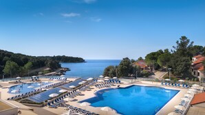 A resort with multiple swimming pools, sun loungers, and umbrellas, overlooking a body of water and surrounded by trees.