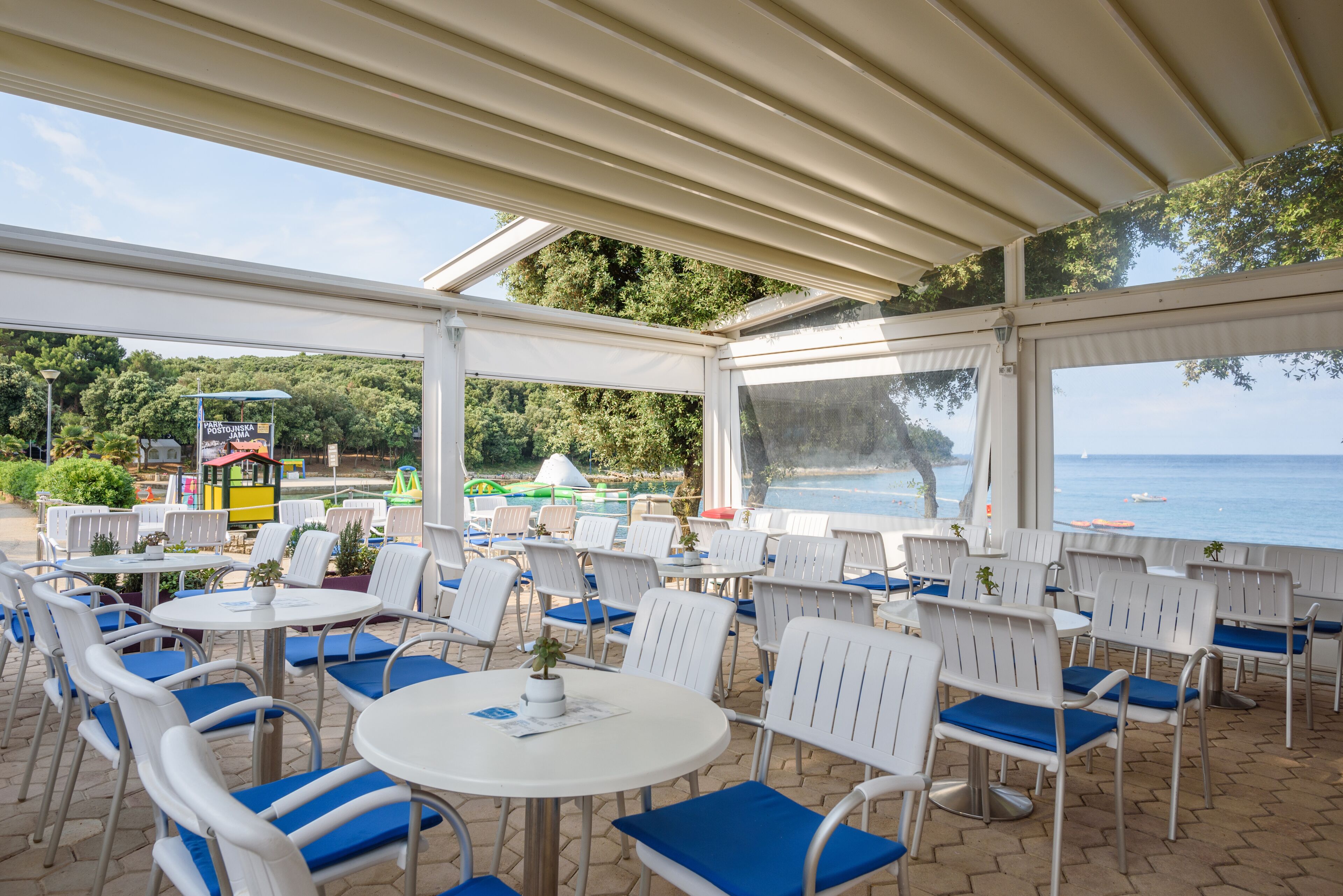 Un patio al aire libre con sillas y mesas blancas, con vistas a una playa y al mar.
