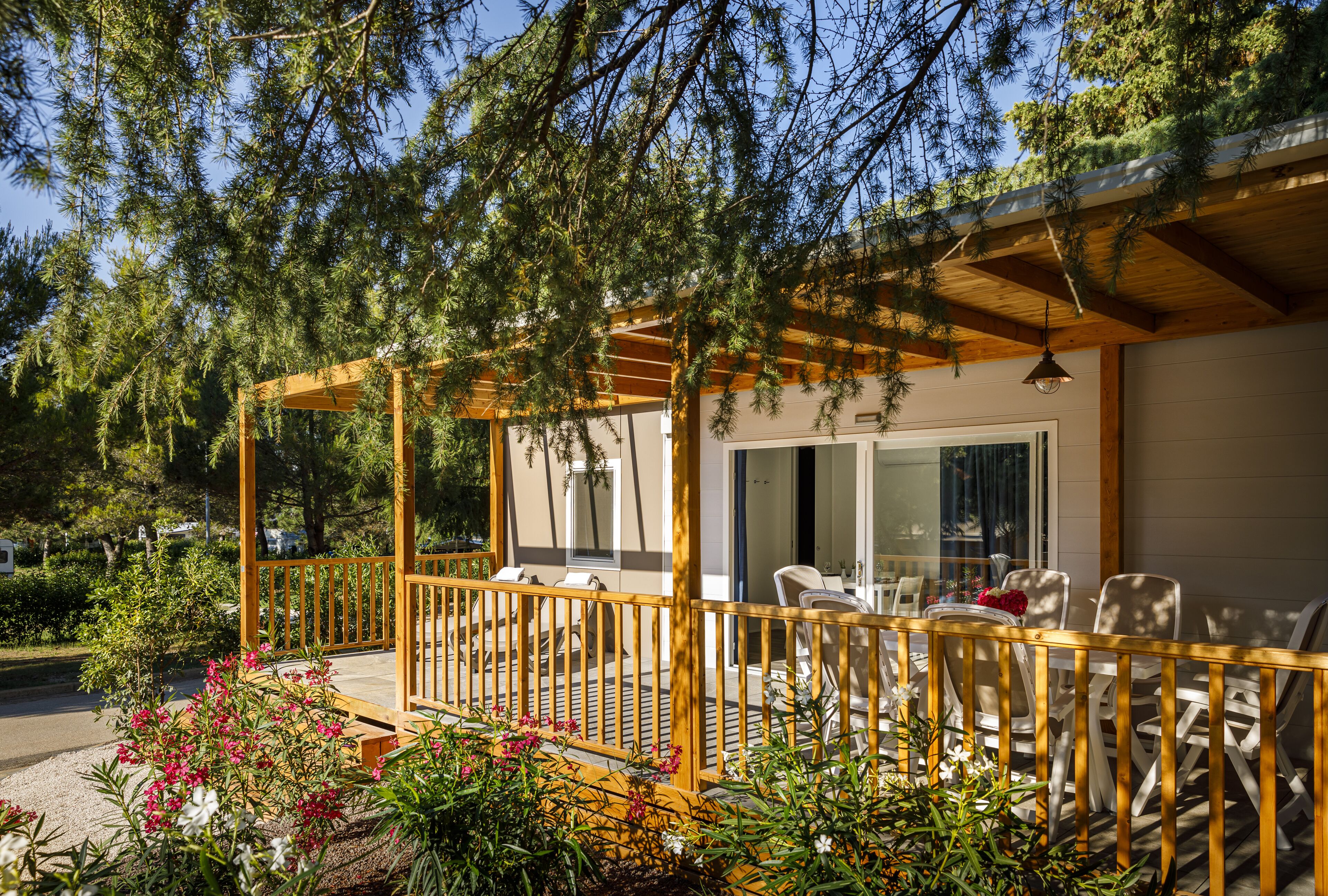 A covered outdoor seating area with wooden furniture, surrounded by lush greenery and flowering plants.