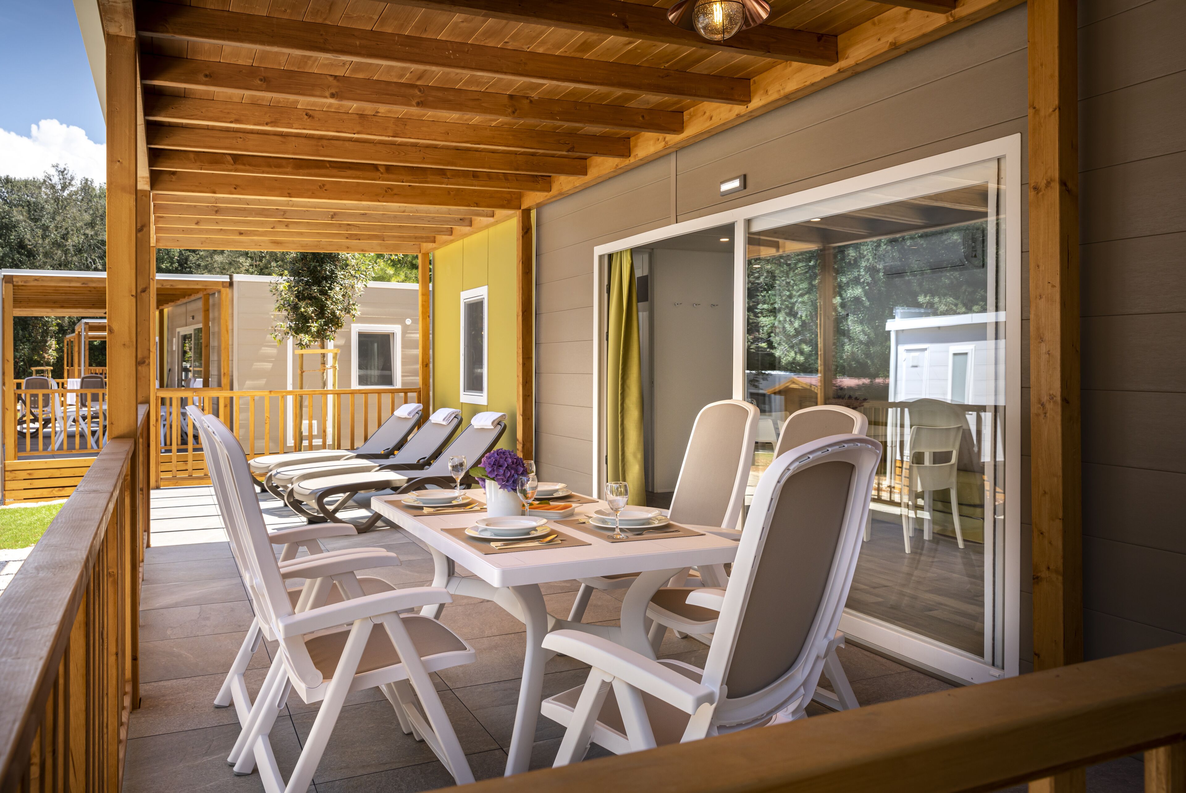 Een overdekt terras met witte stoelen en tafels, een houten terras en uitzicht op de omgeving.