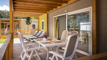 Un'area pranzo all'aperto coperta, con sedie e tavoli bianchi, un molo in legno e vista sul paesaggio circostante.