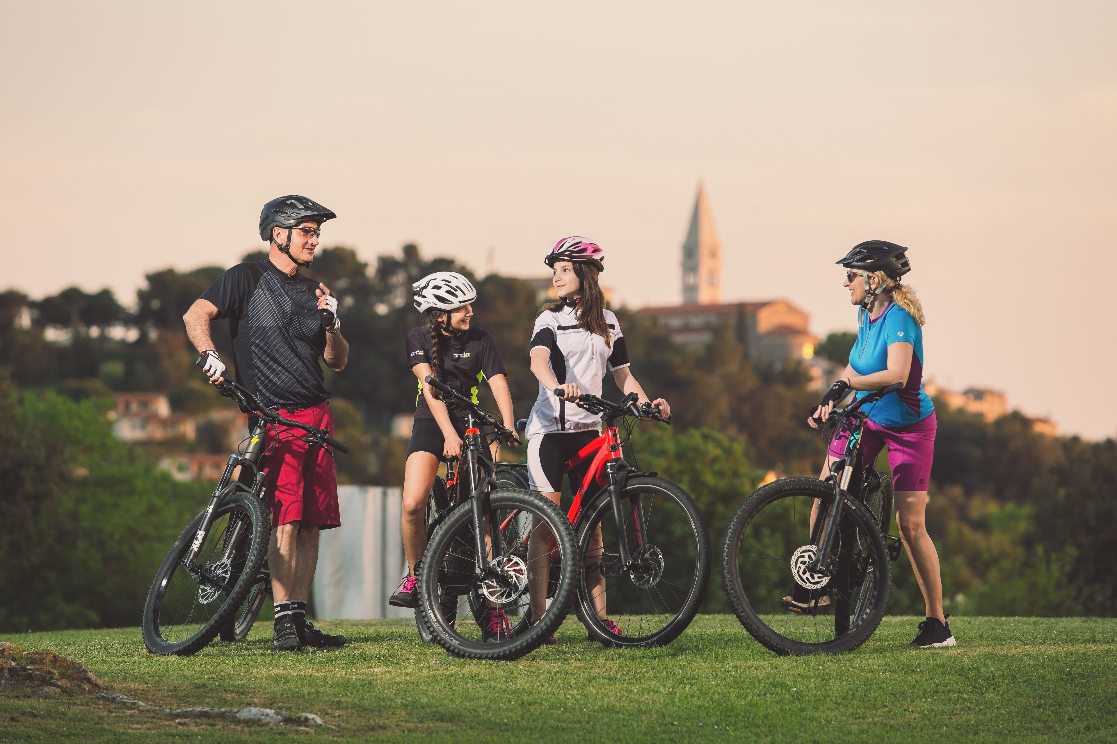 A group of people on bicycles in an outdoor setting with a grassy area and a distant building.