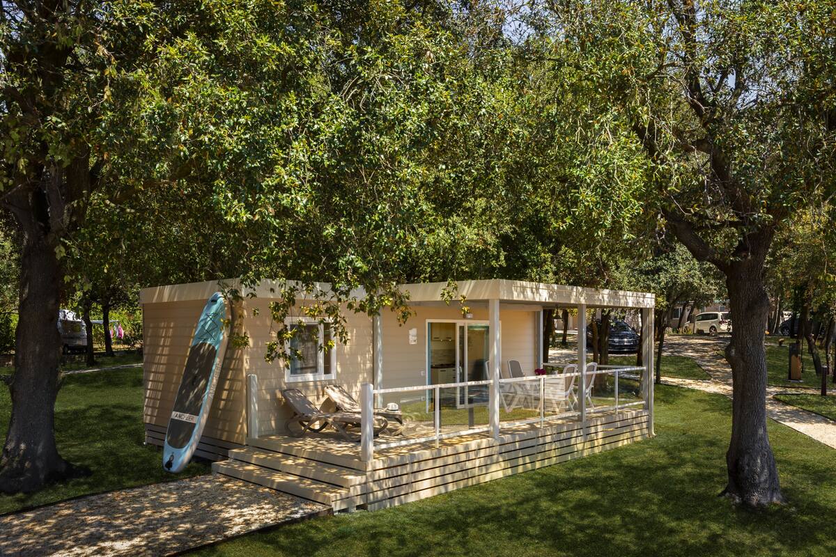 A small, single-story building with a covered patio area, surrounded by trees.