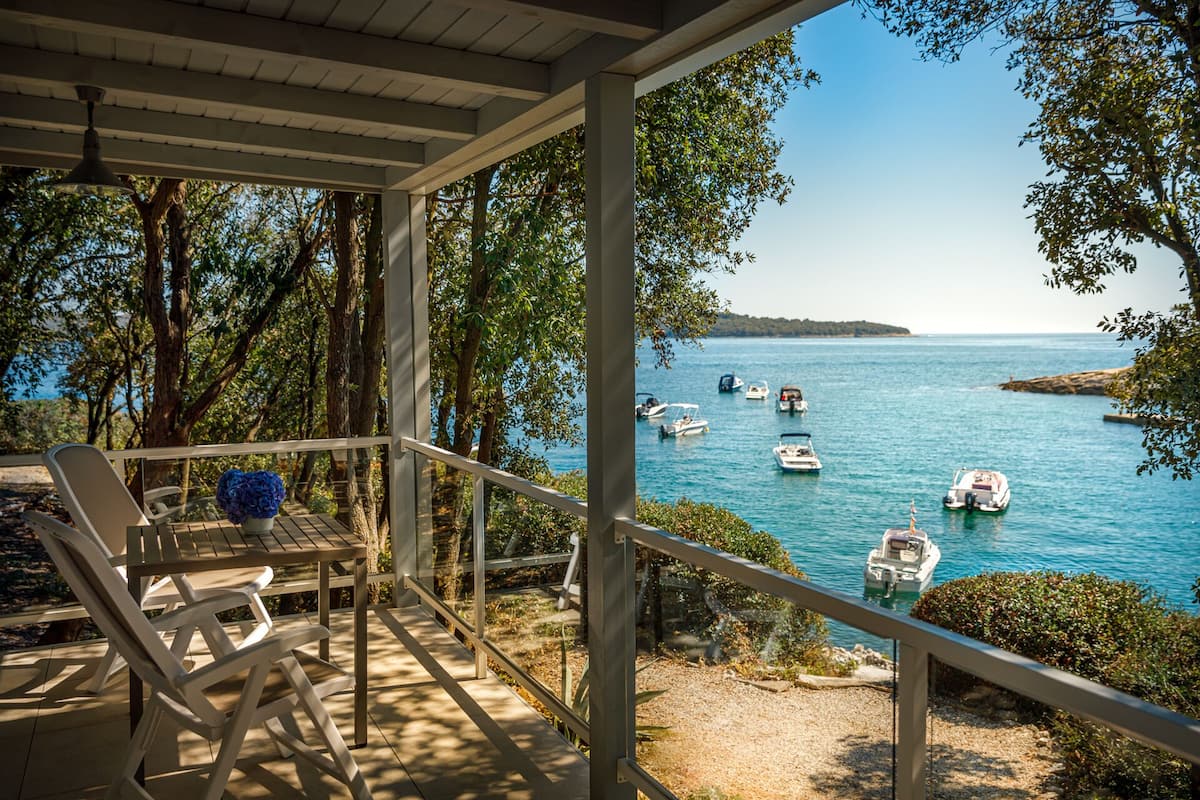 A covered outdoor area with a view of boats on a lake, surrounded by trees.