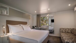 A modern hotel room with a large bed, bedside tables, a sofa, a desk, and a mirror.