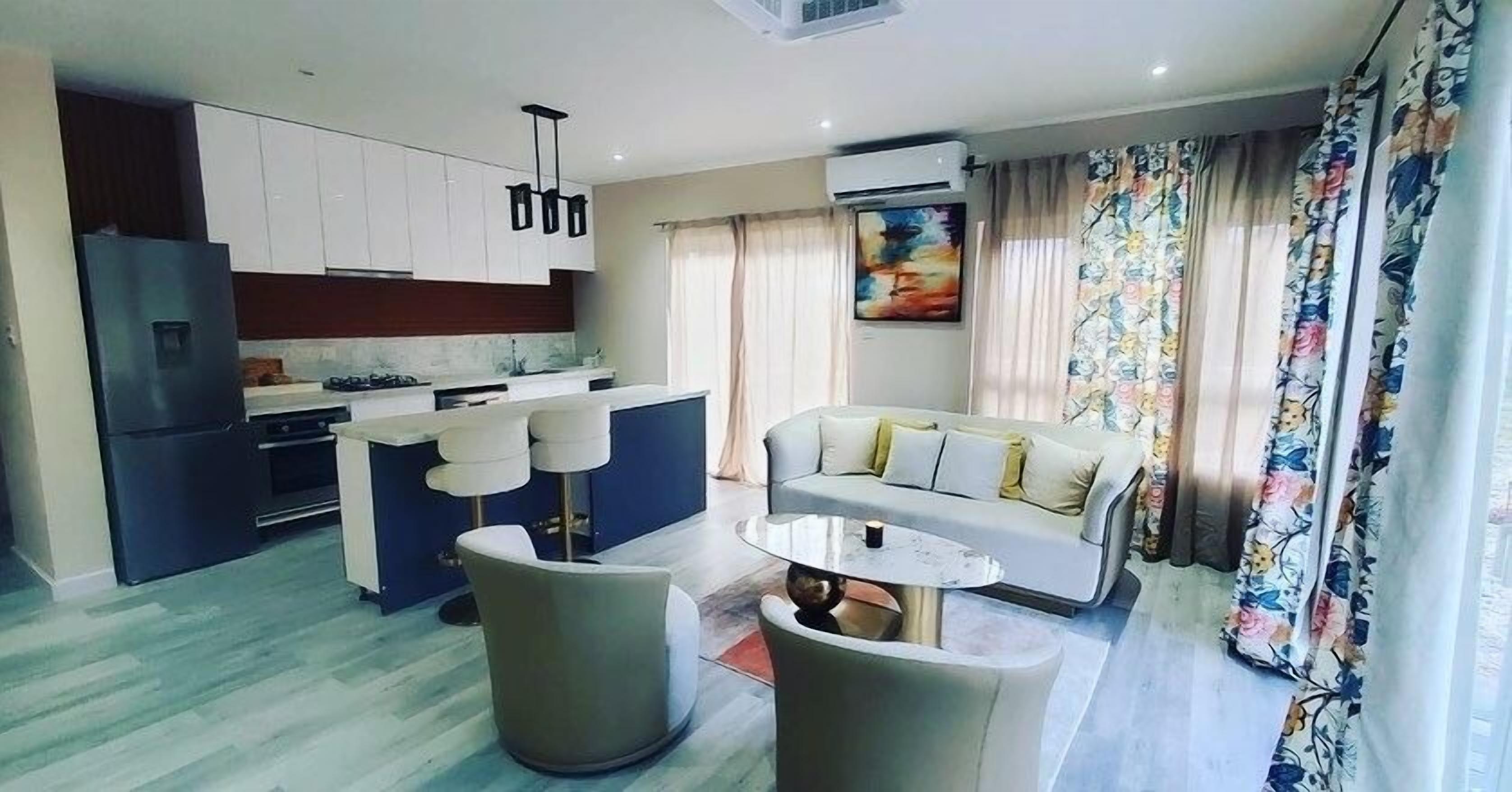Una sala moderna con sofá, una mesa de centro y una zona de cocina con armarios y un refrigerador.