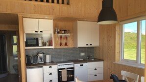 Eine kompakte Küche mit weißen Schränken, einer Mikrowelle, einer Kaffeemaschine und einem Spülbecken. Ein Esstisch mit Stühlen und eine dekorative Pferdestatue sind ebenfalls vorhanden.