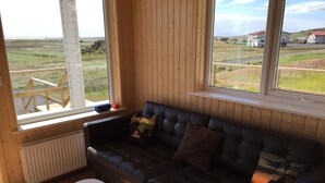 Ein Zimmer mit einem dunkelbraunen Ledersofa, einem weißen Couchtisch und großen Fenstern mit Blick auf eine ländliche Landschaft.