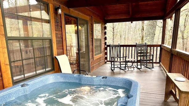 Une terrasse en bois avec un jacuzzi, une table et des chaises.