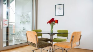 A modern dining area with a glass table, two green cushioned chairs, and a vase with red flowers. - Marimari Apartment, 4th floor with elevator (Split)