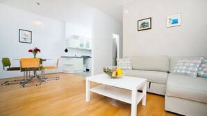 A modern living room with a white sofa, a coffee table with fruit, and a dining area with a chair and table. - Marimari Apartment, 4th floor with elevator (Split)