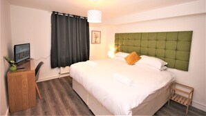 Une chambre d’hôtel avec un lit, un bureau équipé d’un ordinateur, une chaise, une petite table et une fenêtre avec des rideaux.