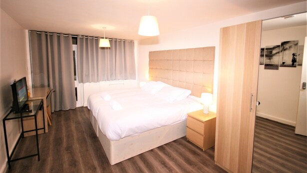 Une chambre d’hôtel avec un grand lit, un bureau avec un ordinateur, une table de chevet avec une lampe et une armoire.
