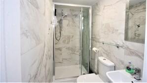 Une salle de bain moderne avec une douche à parois de verre, des toilettes blanches et un lavabo avec un miroir au-dessus.