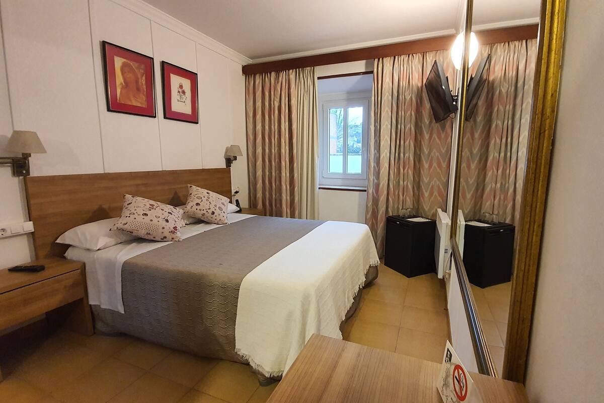 Une chambre d’hôtel comprenant un lit, une table de chevet, une lampe et deux cadres photos fixés au mur.