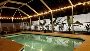 A pool area with a clear pool, lounge chairs, and string lights.