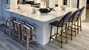 A modern kitchen with a large island, white cabinetry, stainless steel appliances, and striped bar stools.