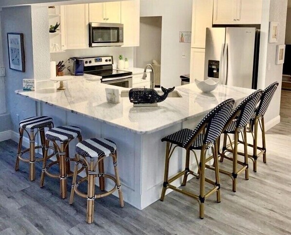 Una cocina moderna con una isla grande, armarios blancos, electrodomésticos de acero inoxidable y taburetes de bar a rayas.