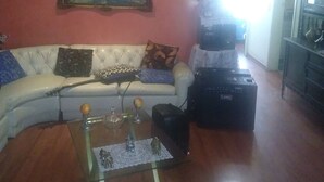 Een woonkamer met een witte bank, een glazen salontafel, een schilderij aan de muur en een zwarte speaker.