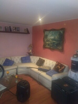 A living room with a white sofa, a glass coffee table, a black speaker, and a painting on the wall.