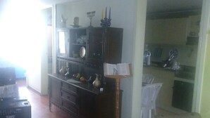 Een woonkamer met een donker houten kast, een eettafel met stoelen, en een keuken die zichtbaar is door een open doorgang.