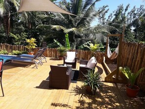 Una terraza de madera con sillones de descanso, una mesita y una hamaca.