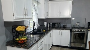 A compact kitchen with white cabinets, a granite countertop, a stove, and a microwave. - The Island Experiences-Samo (Choiseul)