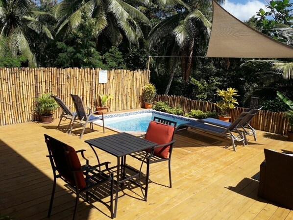 Una terraza de madera con piscina, rodeada por una valla de bambú y palmeras.