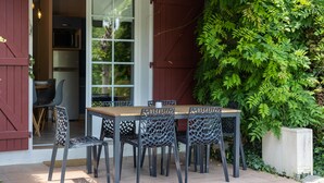 Zona pranzo all'aperto con tavolo e sedie, una porta rossa e vista su piante.
