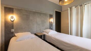 A hotel room with two single beds, a small wooden nightstand, and two wall-mounted light fixtures.