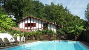 Una piscina con lettini e una casa con persiane rosse.