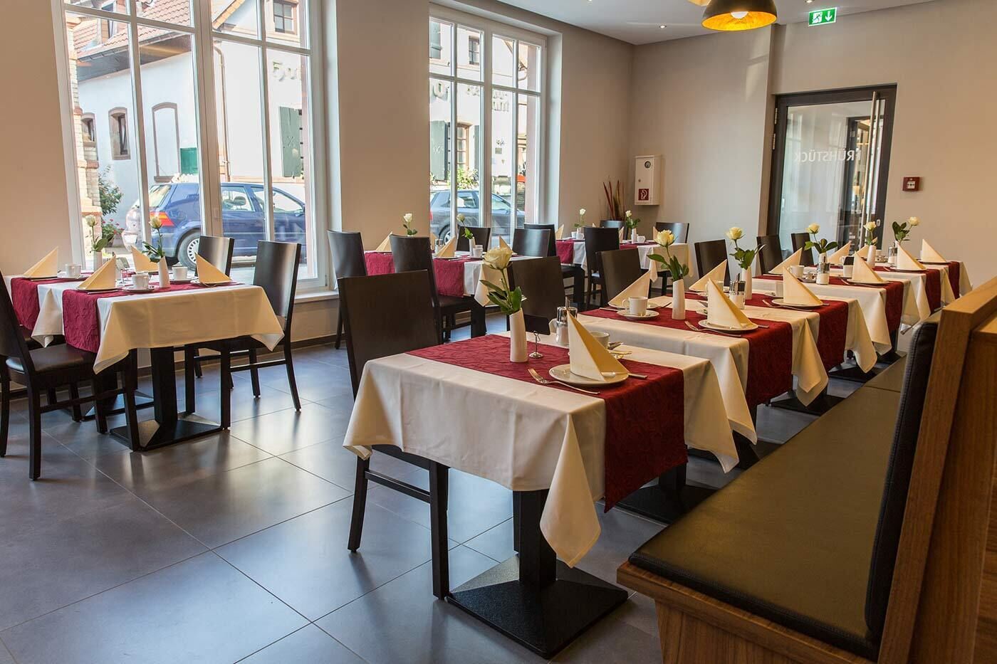 A restaurant with multiple tables set for dining, large windows, and a view of the street outside.