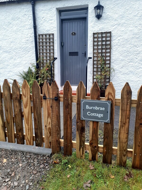 A wooden fence with a sign reading "Burnbrae Cottage."