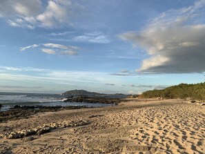 Una playa con costa rocosa, una montaña distante y cielo despejado.