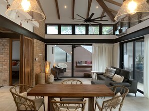 Una habitación amplia con una mesa de comedor de madera, sillas de mimbre, un sofá gris y un ventilador de techo.
