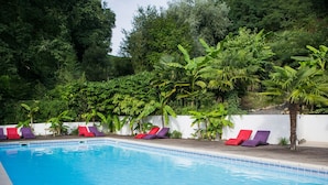 Une piscine entourée de chaises longues et d’une végétation luxuriante.