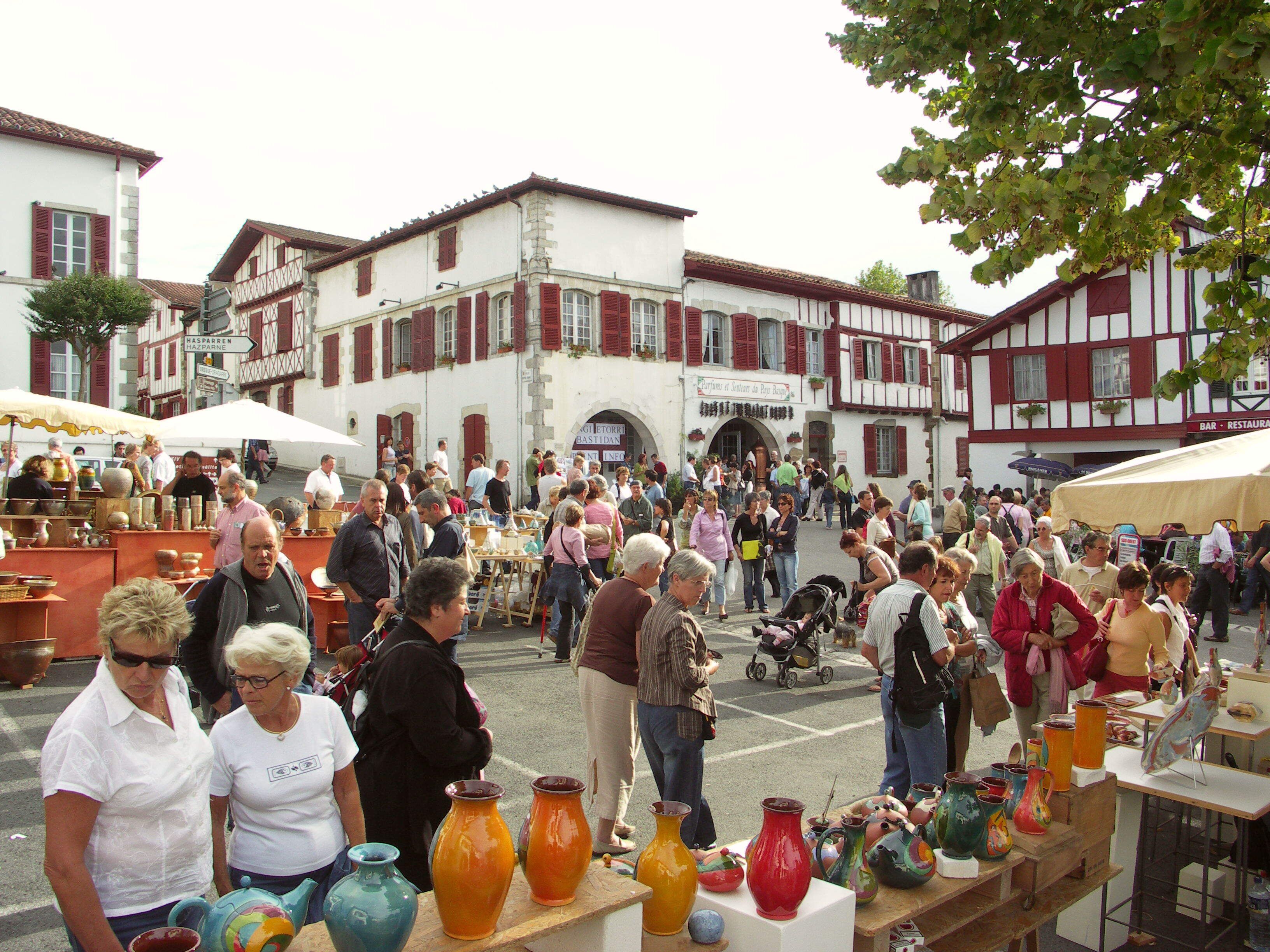 Un marché animé en plein air, où les gens flânent et les vendeurs proposent de la poterie.