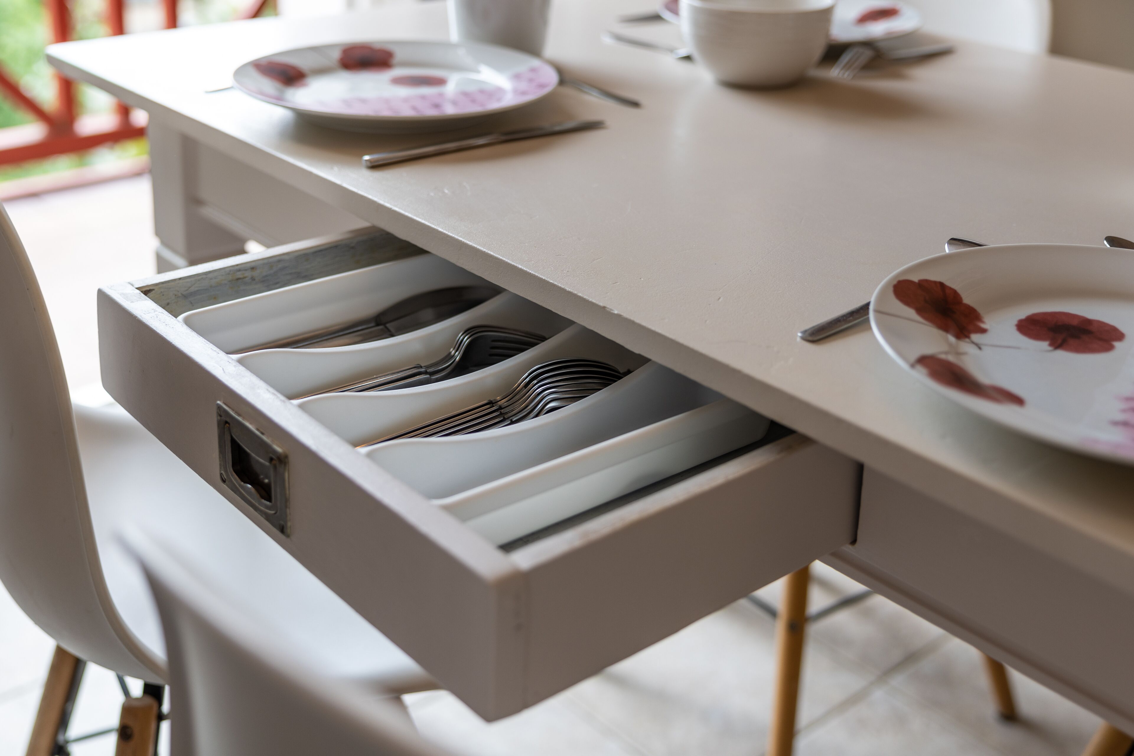 Una mesa de comedor con un cajón que contiene utensilios.