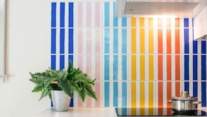 Une cuisine avec un plan de travail blanc, une cuisinière et un crédence colorée à rayures.